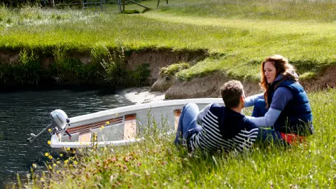 Due persone sedute sulla riva di un fiume accanto a una barca in acqua.